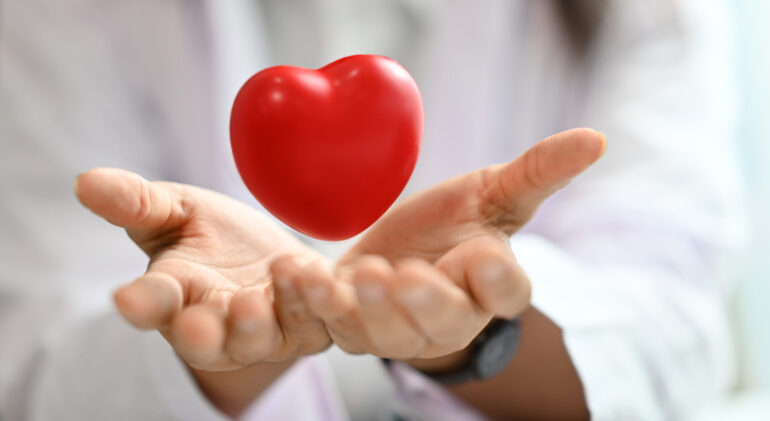 Red heart floating over opened hands. Health care, cardiological, medical and charity concept.